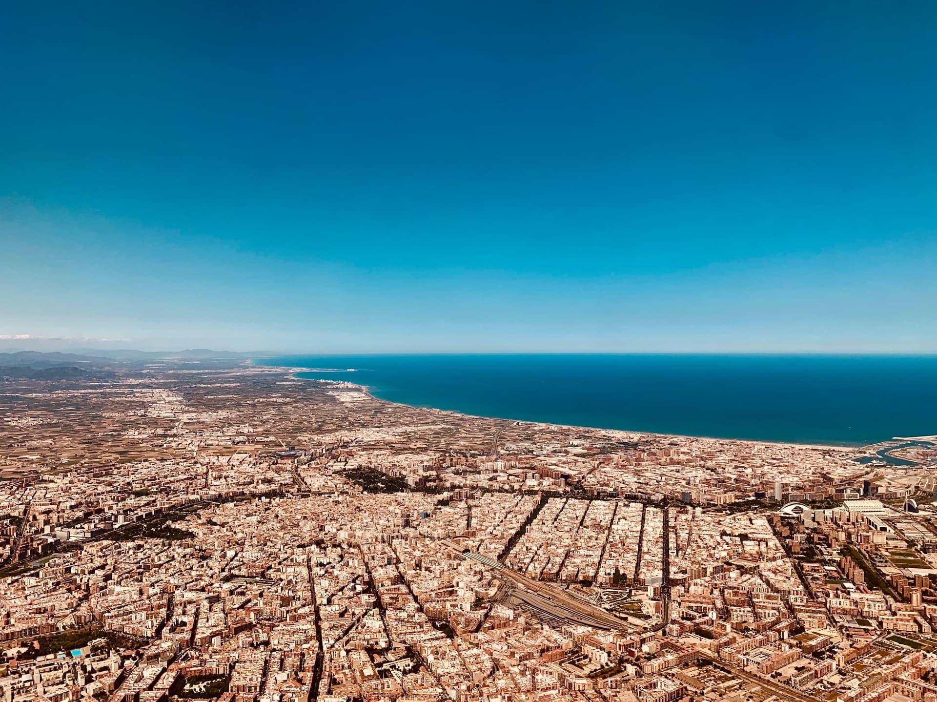 Luchtfoto van Valencia: de stad loopt door tot aan de kust, met de zee rechts en een heldere lucht erboven.