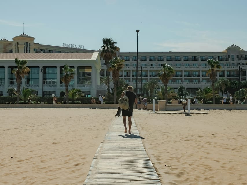 Houten looppad over het zand, met het Las Arenas-hotel op de achtergrond.