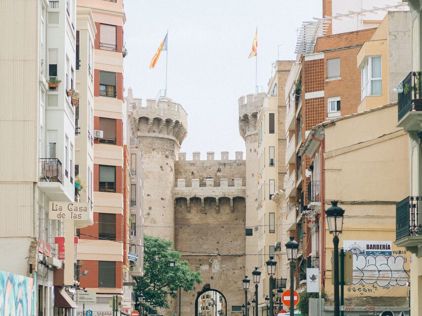 De Torres de Quart aan het eind van een rechte straat, met twee vlaggen van de Valenciaanse Gemeenschap erbovenop en gebouwen aan weerszijden.